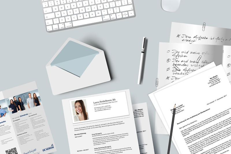 Büromaterialien und Dokumente auf hellblauem Hintergrund, darunter Tastatur, Stift, Notizen und Bewerbungsunterlagen.